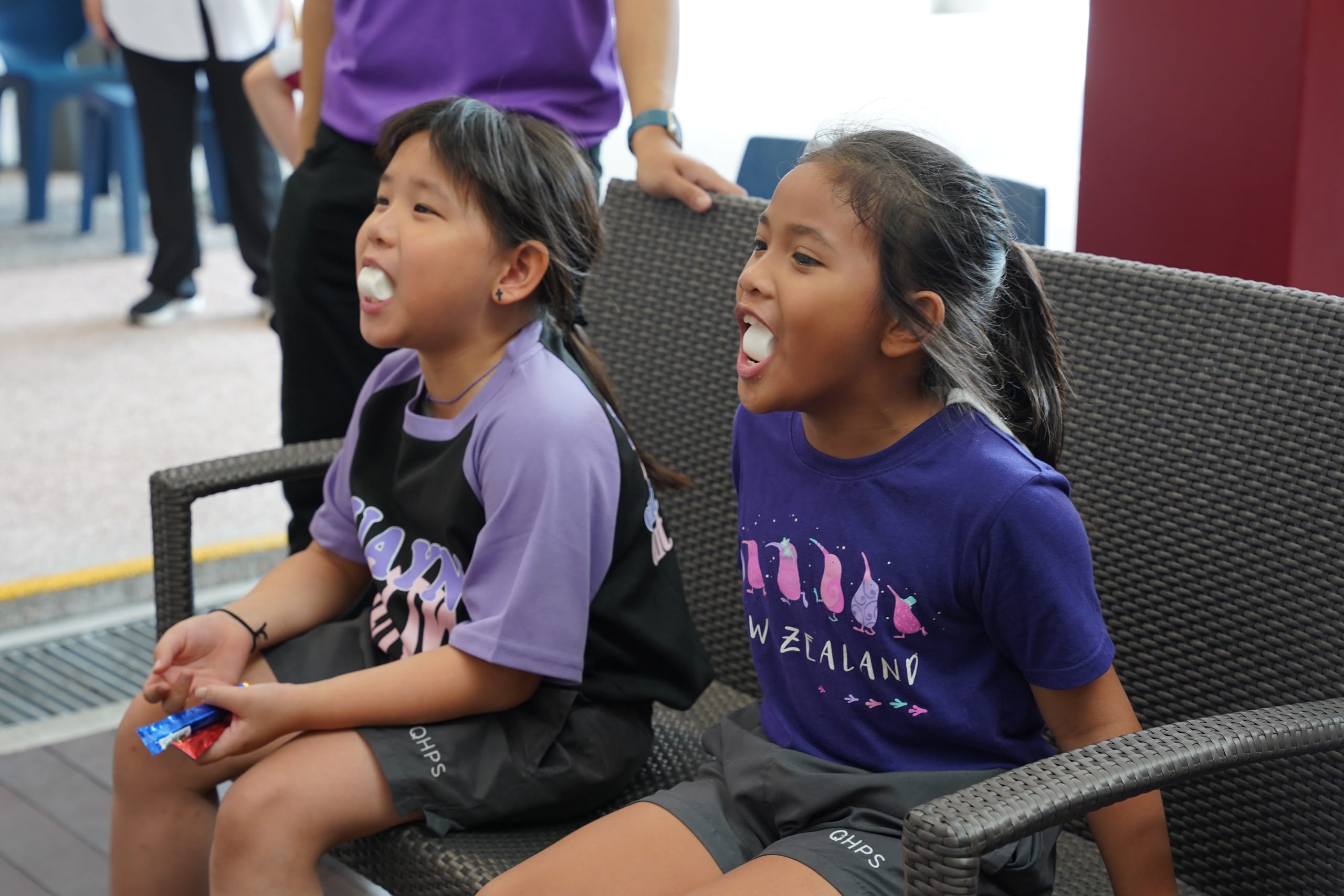 Two girls putting marshmallows in their mouth while trying to speak